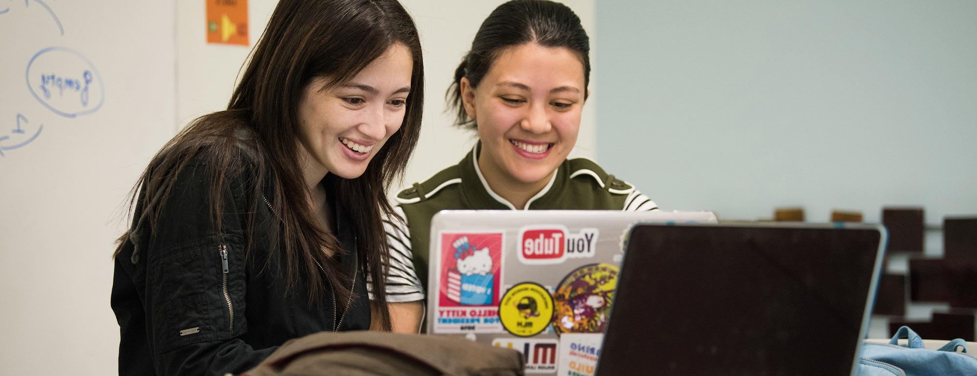 两名女学生共用一台笔记本电脑来评估她们的工作.