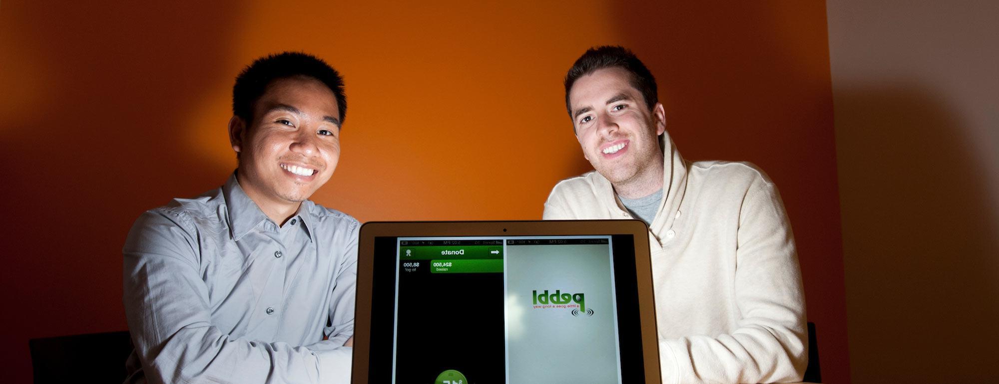 Two Graduate students pose with a laptop that shows the app that they created.