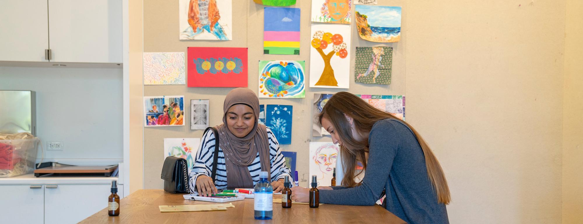 在amjs澳金沙门，两名学生在一张被艺术品包围的桌子旁工作. 