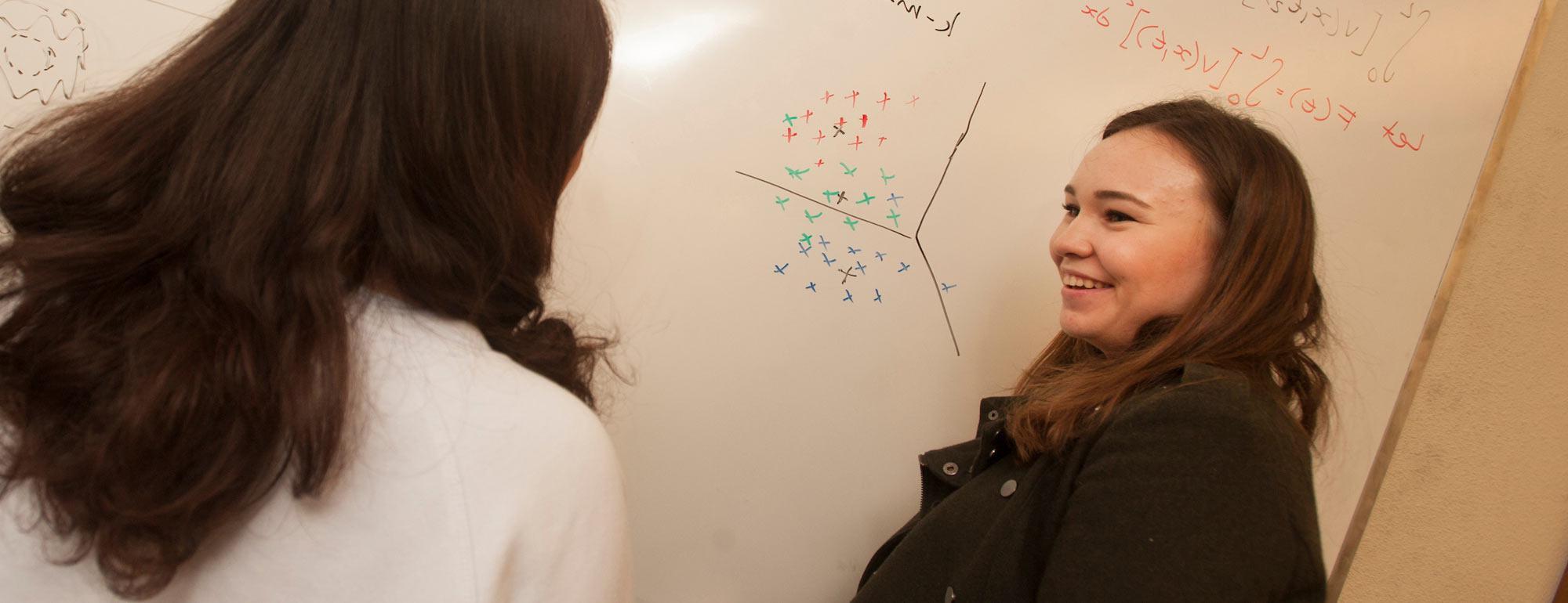 两个女学生在白板上讨论一道数学题